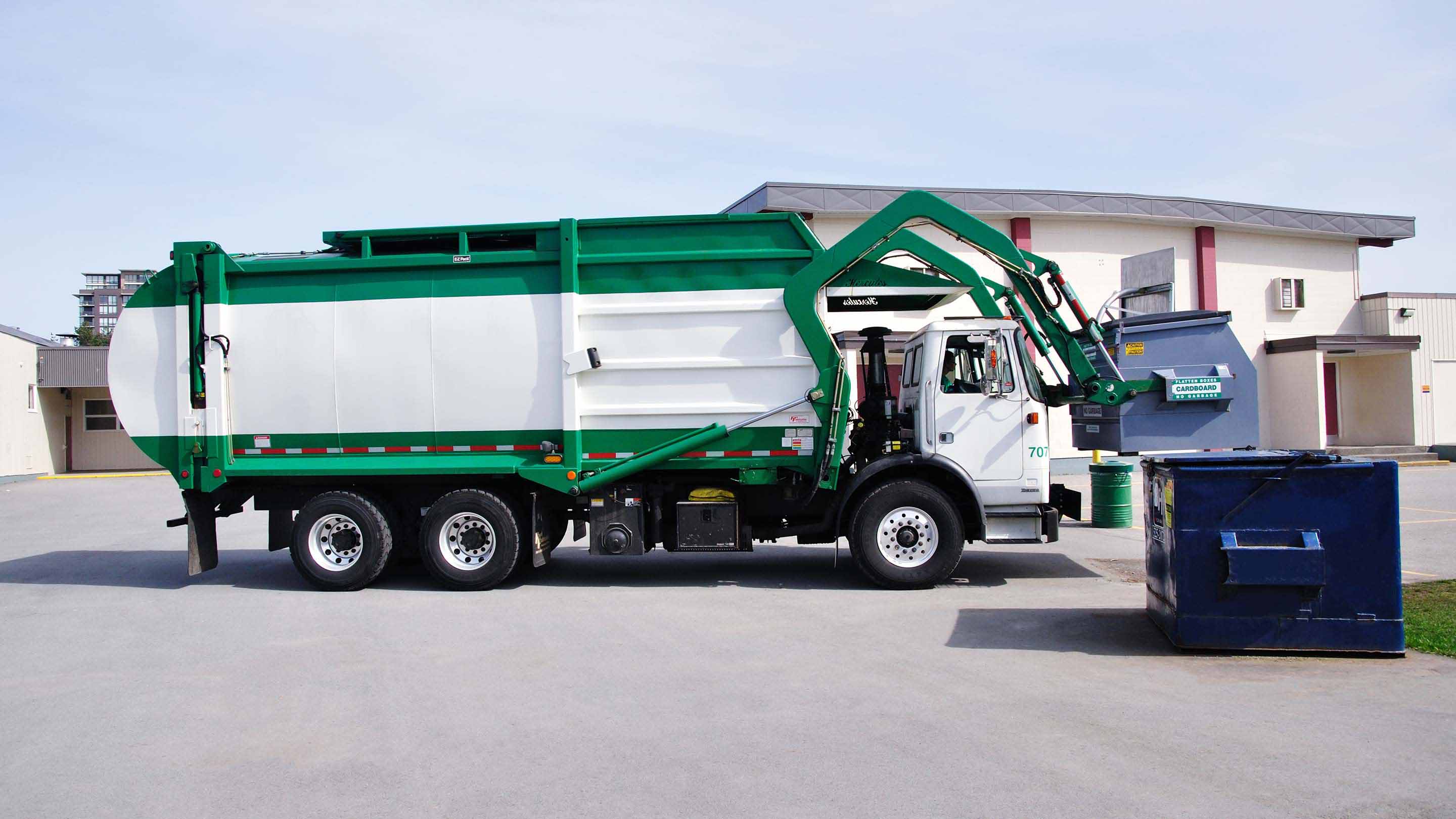 Camion della spazzatura verde e bianco che solleva un cassonetto blu