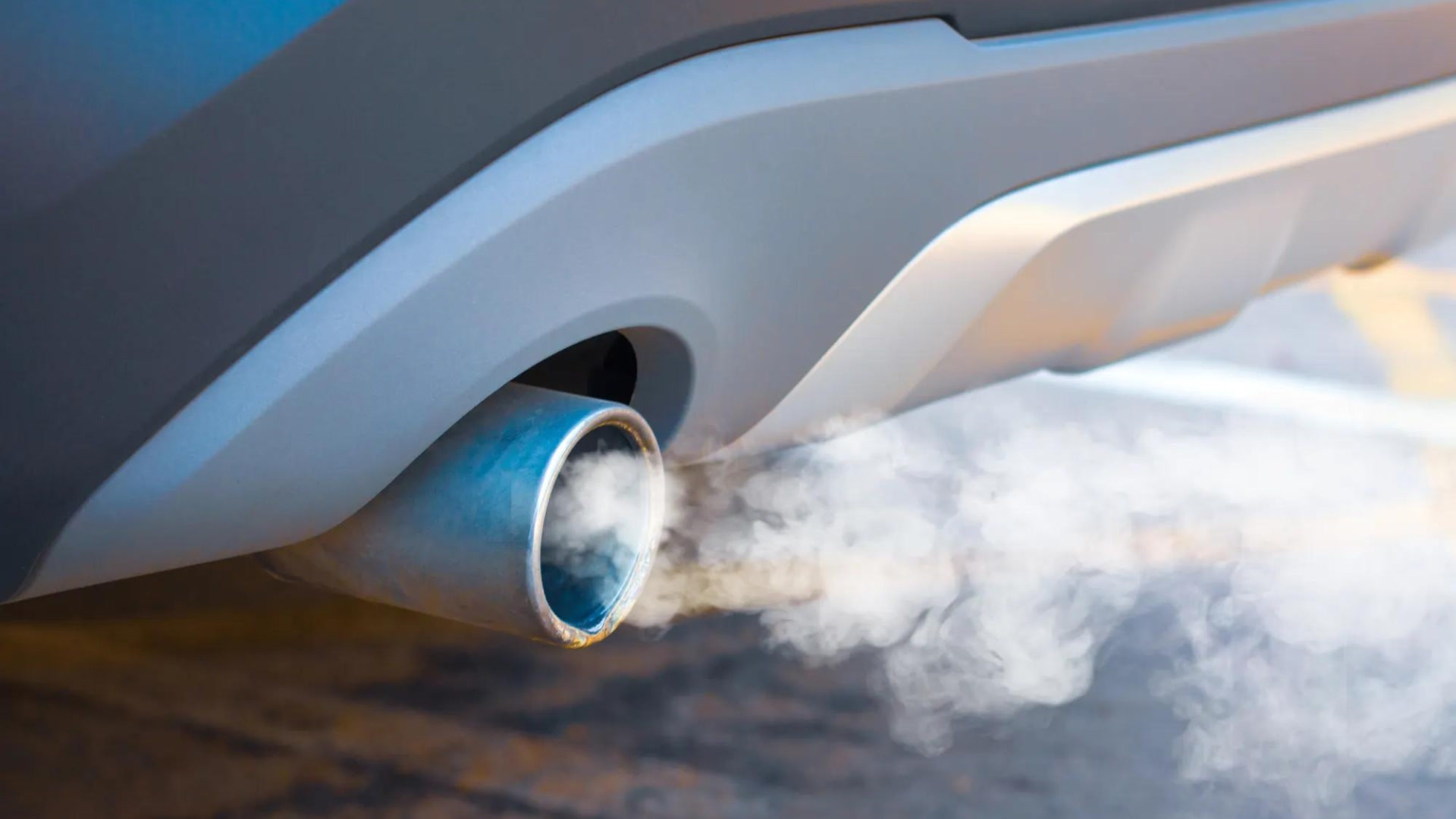 Close-up of a vehicle's exhaust pipe emitting white smoke with a blue-tinted interior visible