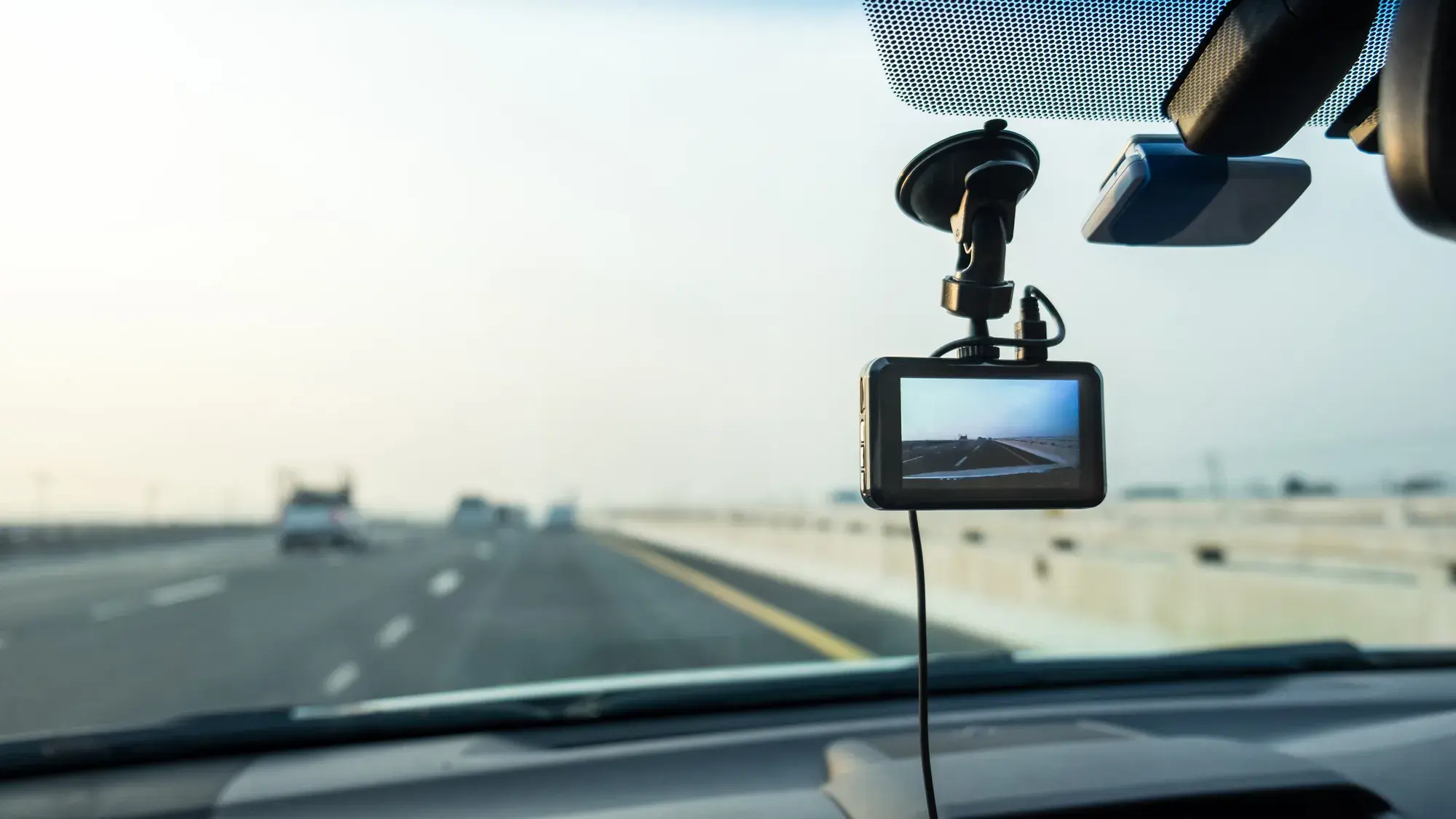 A dashcam mounted on a vehicle windshield records the highway ahead with other cars visible in the distance