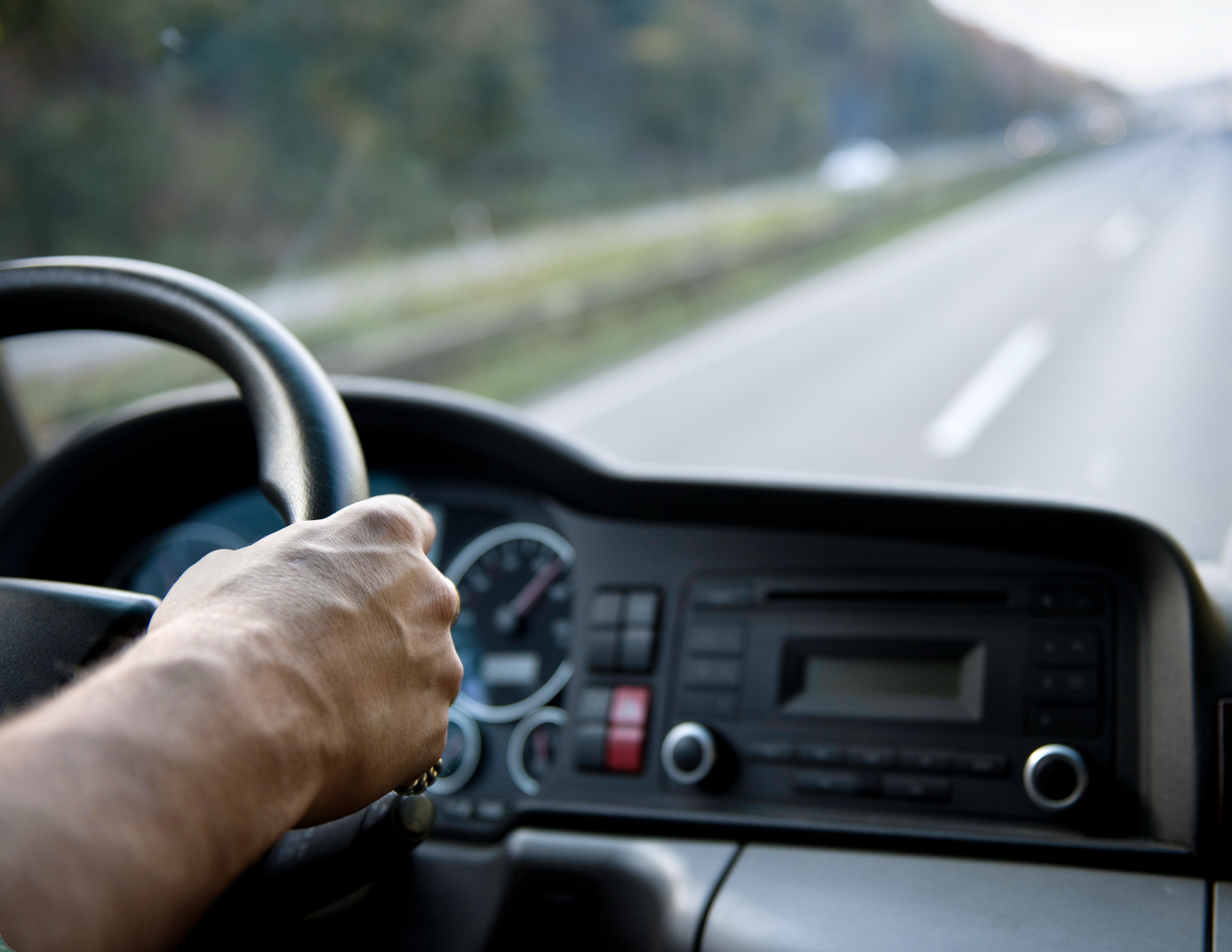 De hand van een chauffeur die een stuur vastgrijpt in een voertuig.