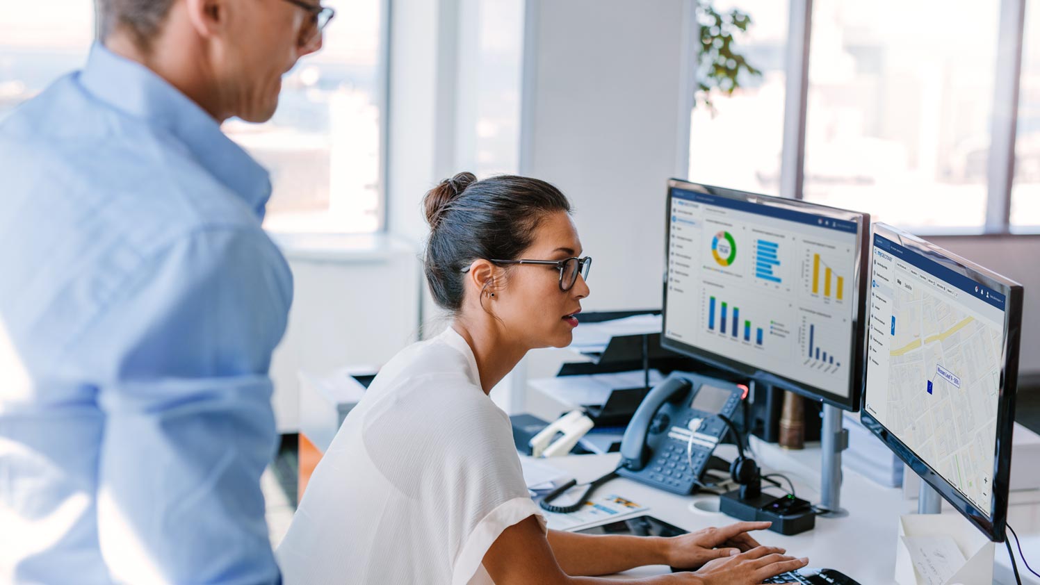 Woman working on two monitors displaying MyGeotab dashboards