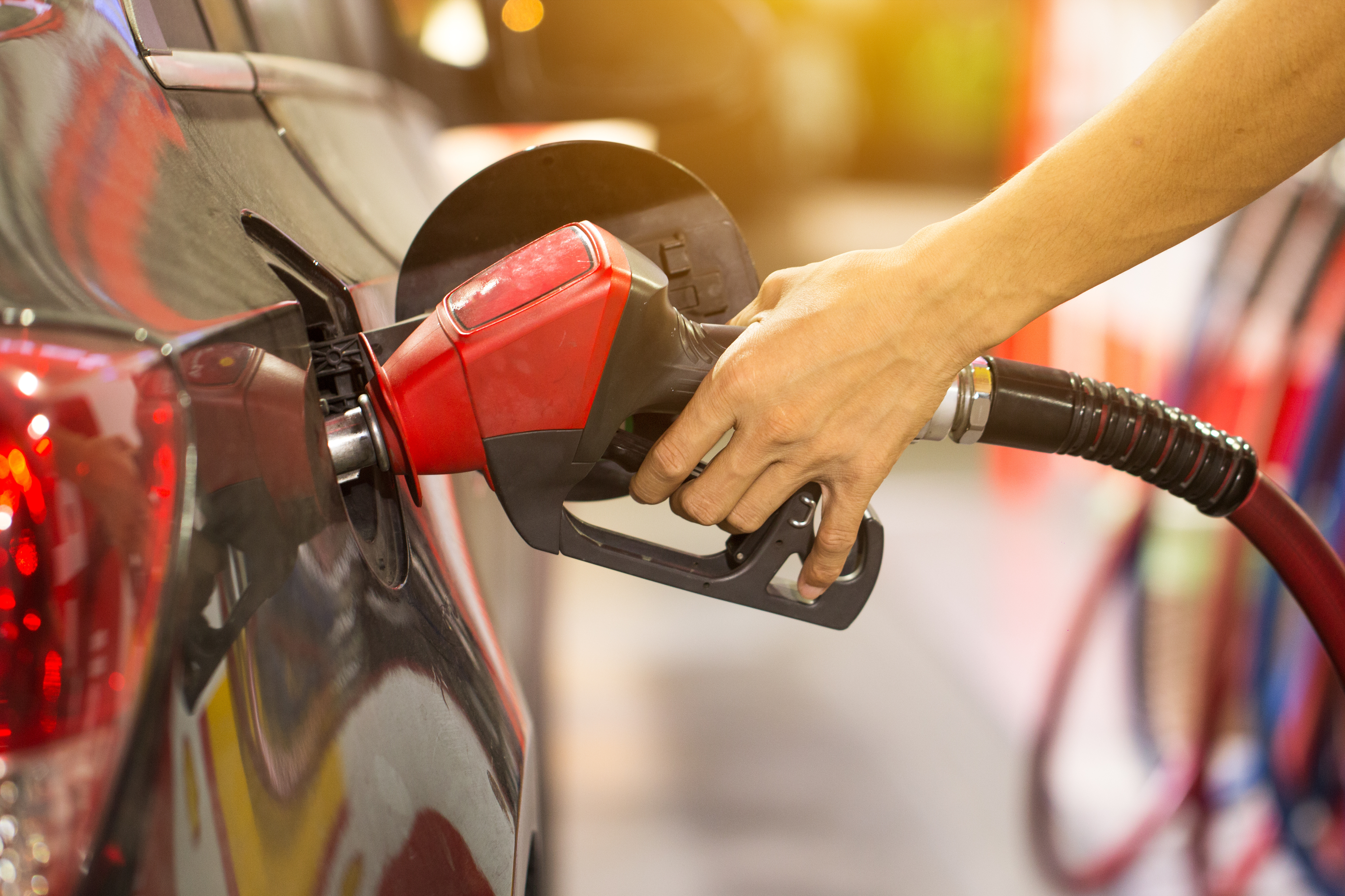 A hand holding a fuel pump nozzle refuelling a dark car at a petrol station.
