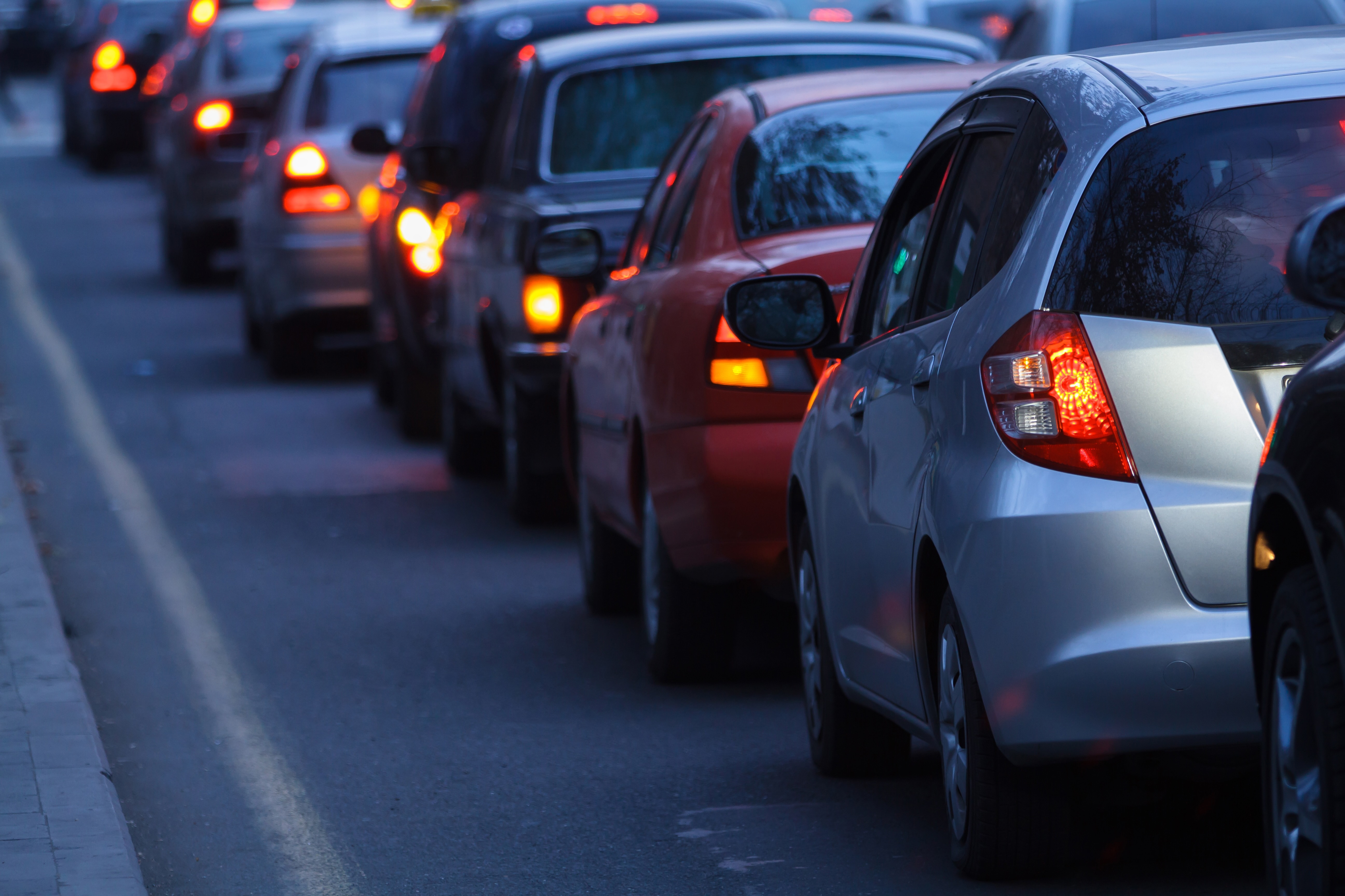A close-up view of heavy, bumper-to-bumper traffic with illuminated red brake lights, illustrating severe road congestion.