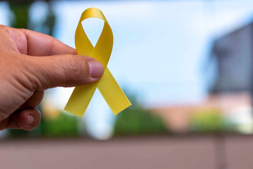 Mão segurando um laço amarelo, símbolo da campanha Maio Amarelo, que representa a conscientização para a segurança no trânsito. Ao fundo, o cenário está desfocado, dando destaque ao laço.