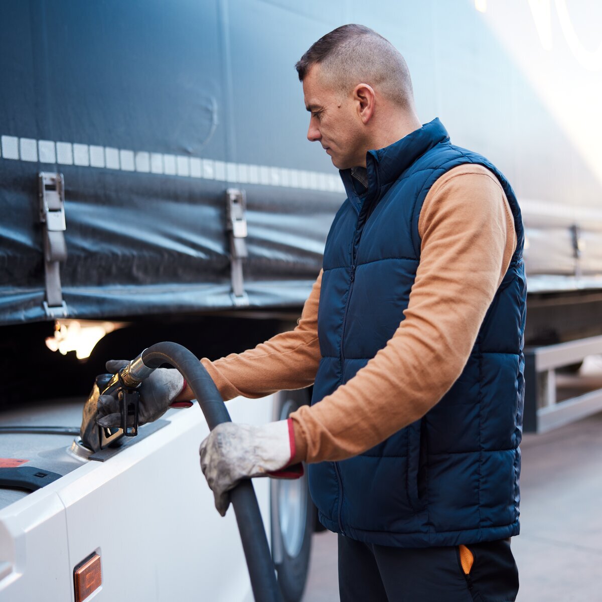 Motorista de caminhão de transporte pesado abastecendo o veículo com combustível em um posto.
