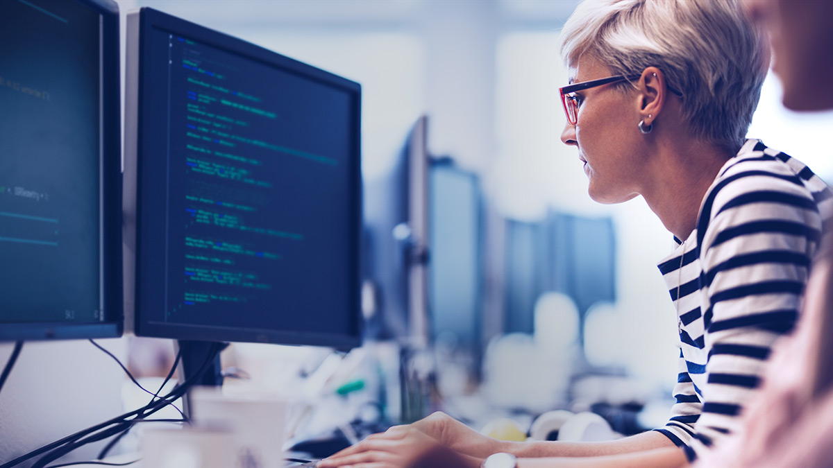 A woman writing code, sitting in front of a computer monitor. 