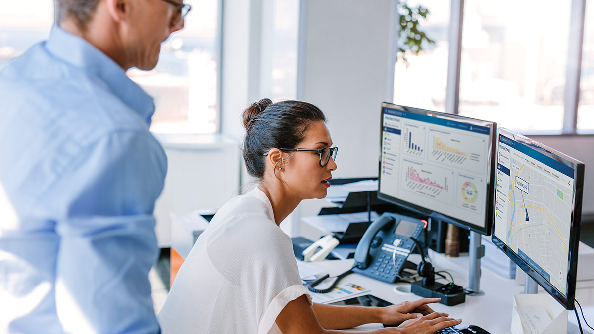 Mujer trabajando en dos monitores que muestran paneles de gráficos de MyGeotab