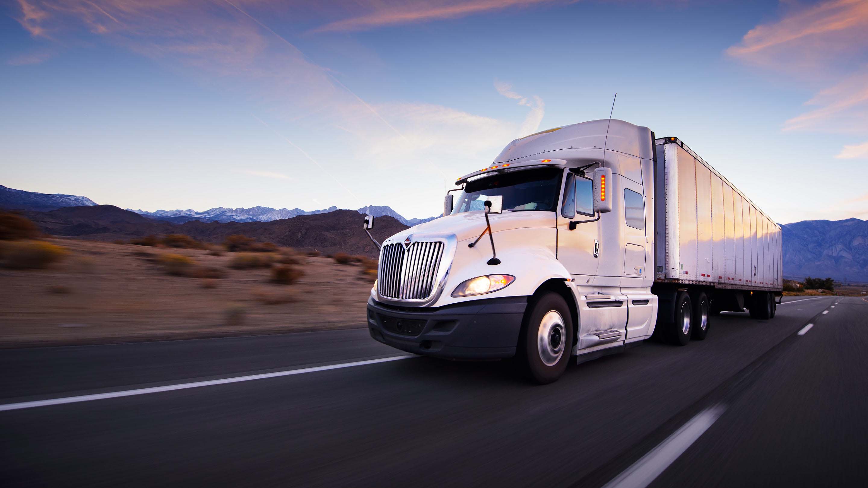 Truck driving on a highway with mountains in the background