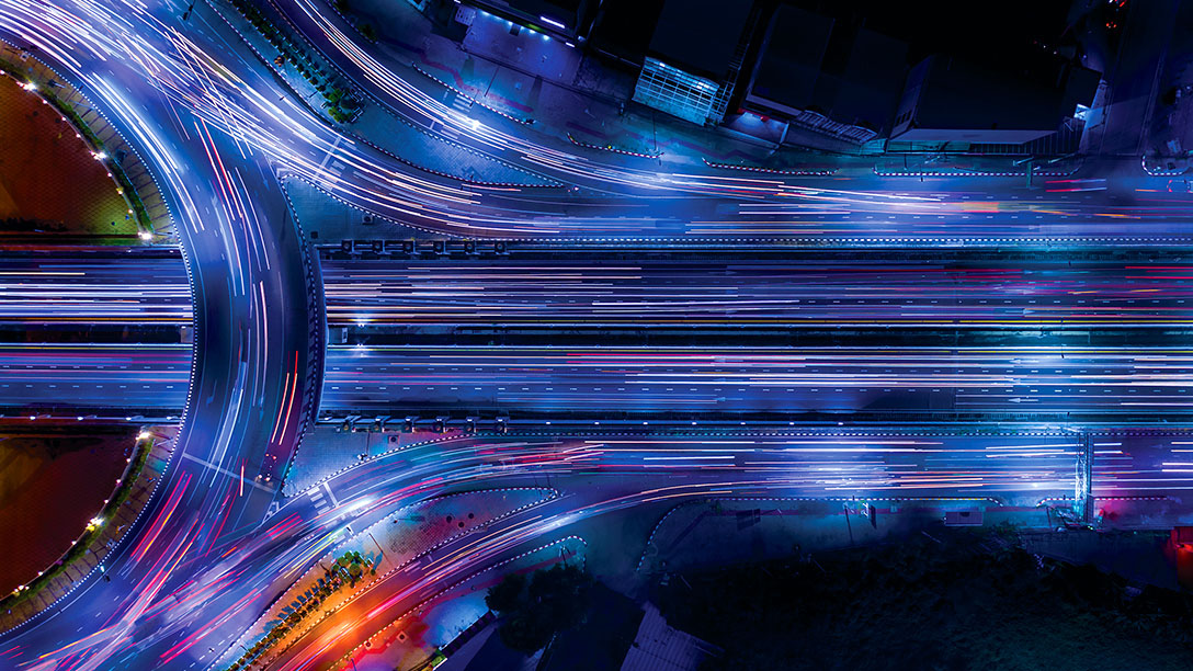 Fast forwarded image of vehicles driving on a blue and purple lighted road at night.