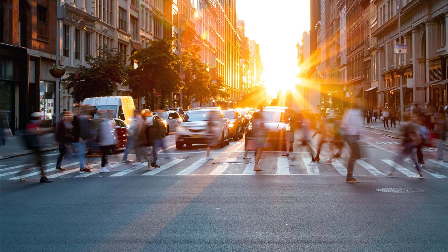 People crossing busy street with sunset in the background