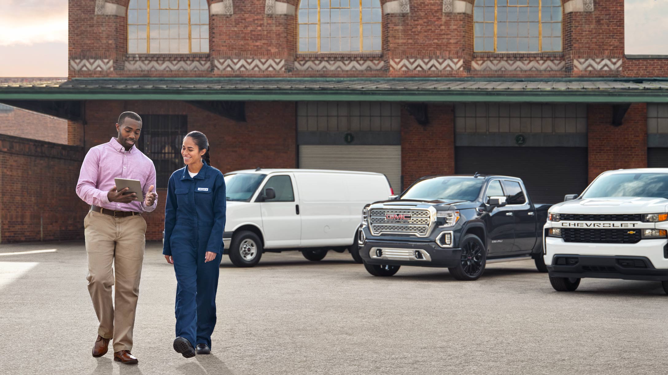 two people walking and talking in a parking lot with vehicles in the background