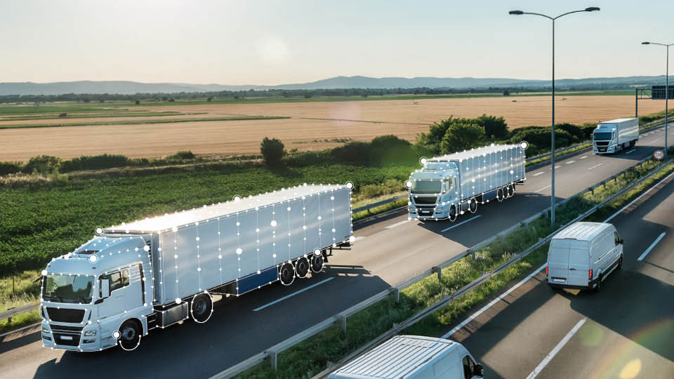 Semi trucks and vans with data points driving on a two-way highway with fields in background