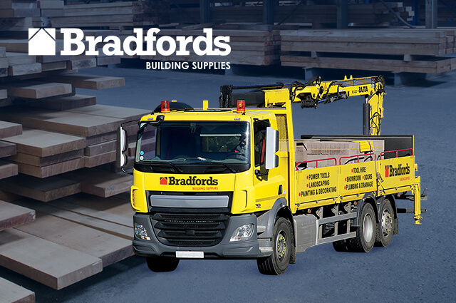 Yellow truck that loads cargo with lumber in background and company logo in the left hand corner. 