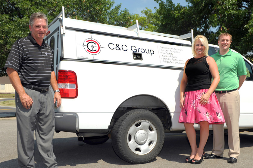 Three people standing in front of a C&C branded pickup truck