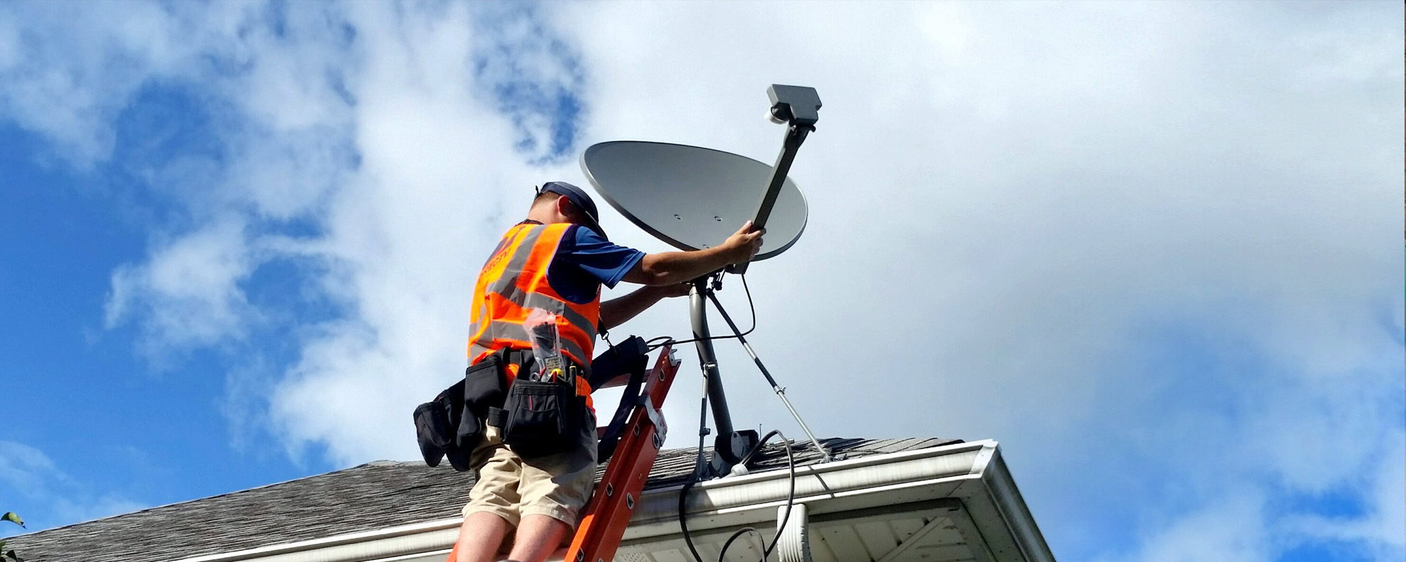 Man wearing an orange safety vest on a roof installing a satellite dish