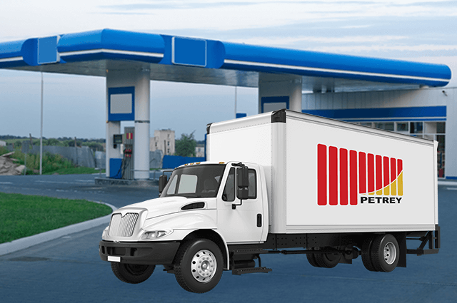 White delivery box truck with PETREY's  company logo on it and blue gas station in the background. 