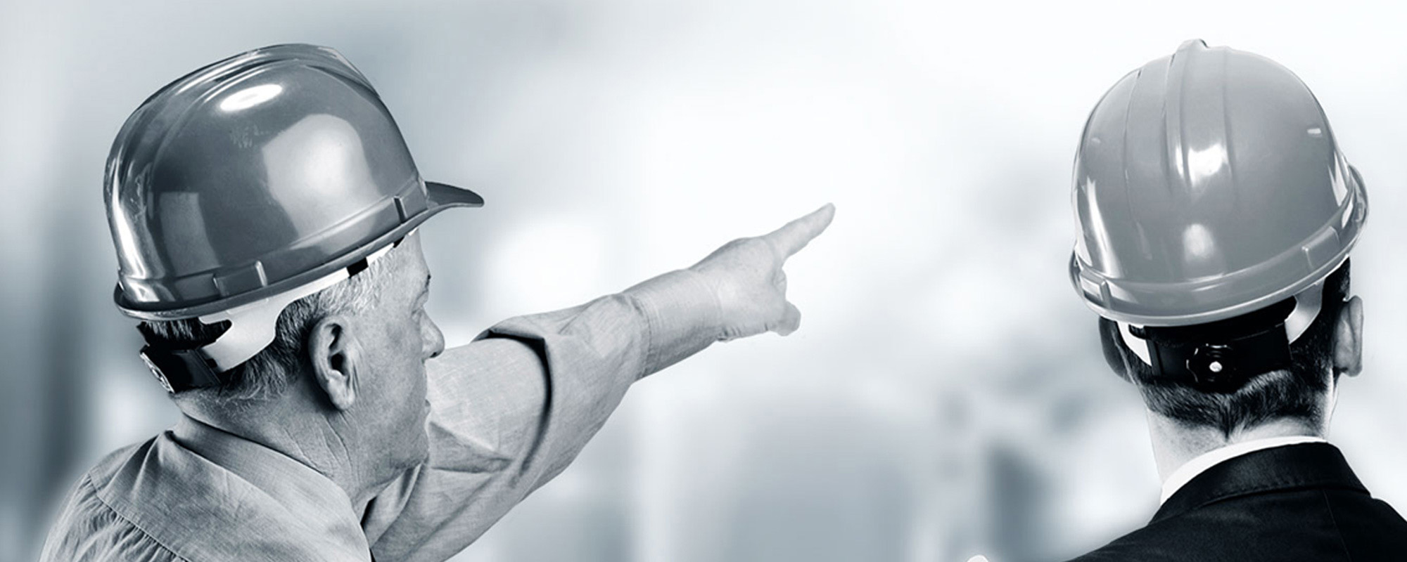 A black and white photo of two men in hard hats. One is pointing into the distance