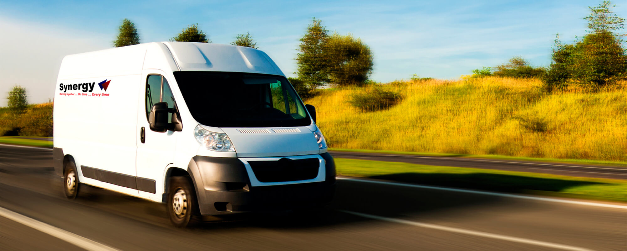 A white delivery van driving on a road with the Synergy Courier Services logo on it