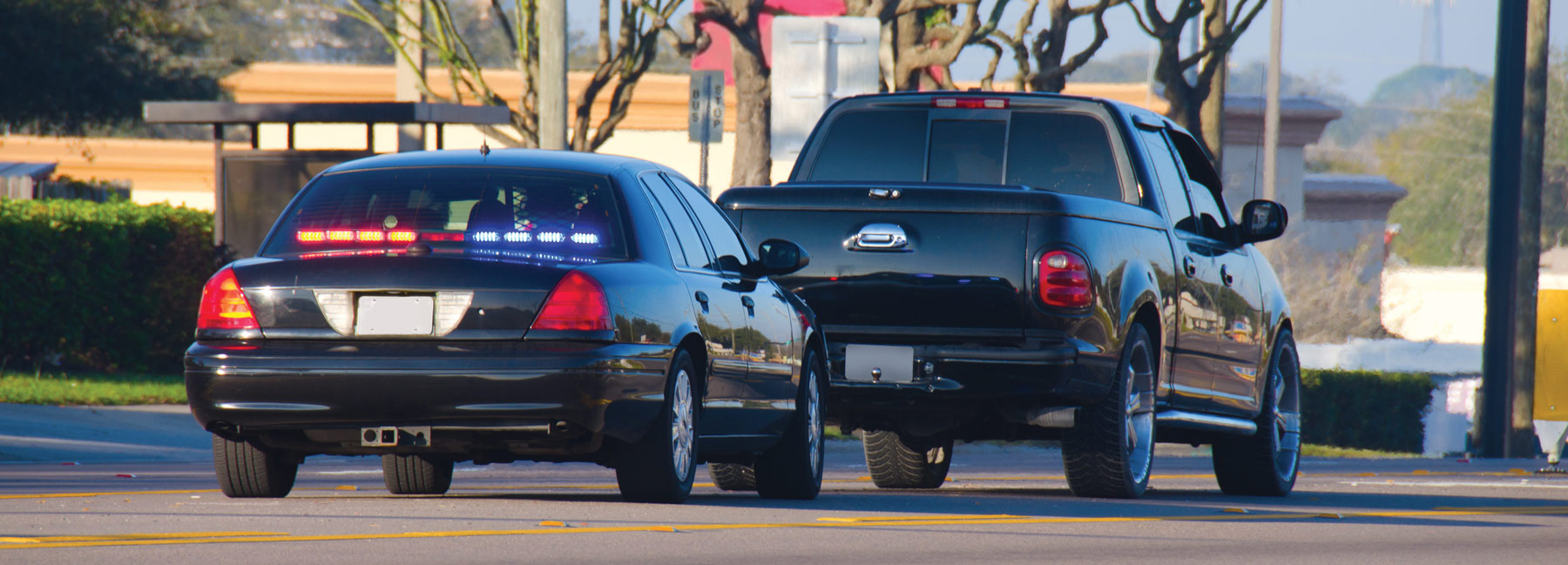 Back of black police car with red and blue lights flashing stopping a black van