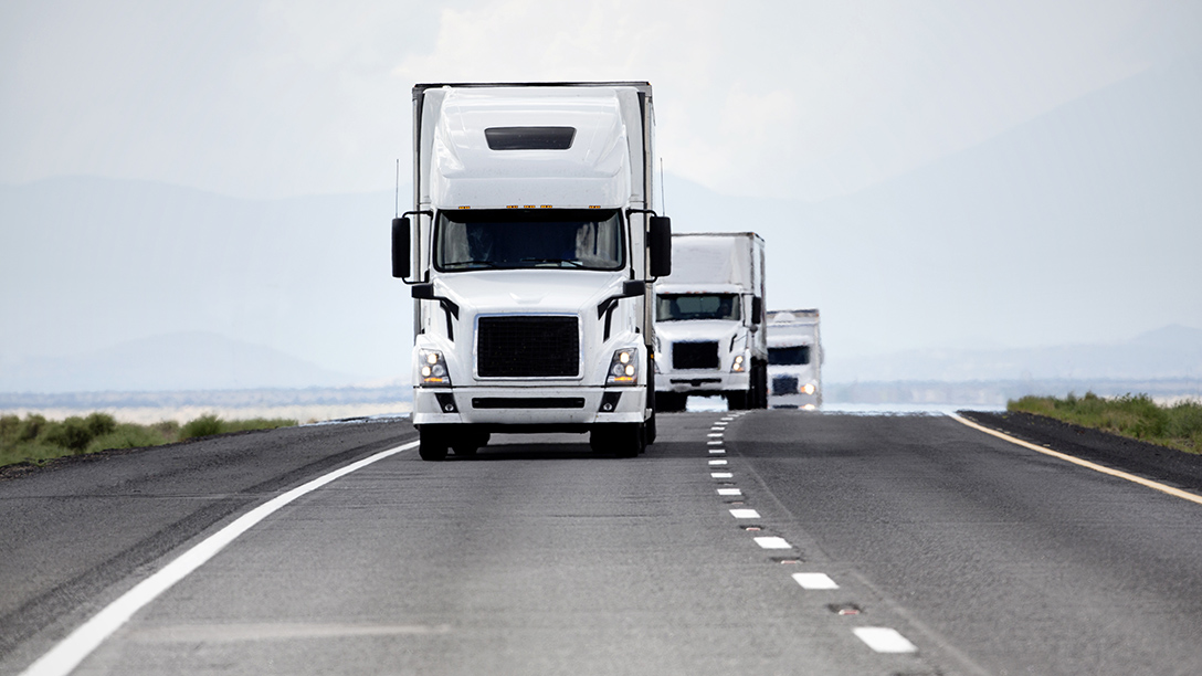 Three white trucks platooning down an open road