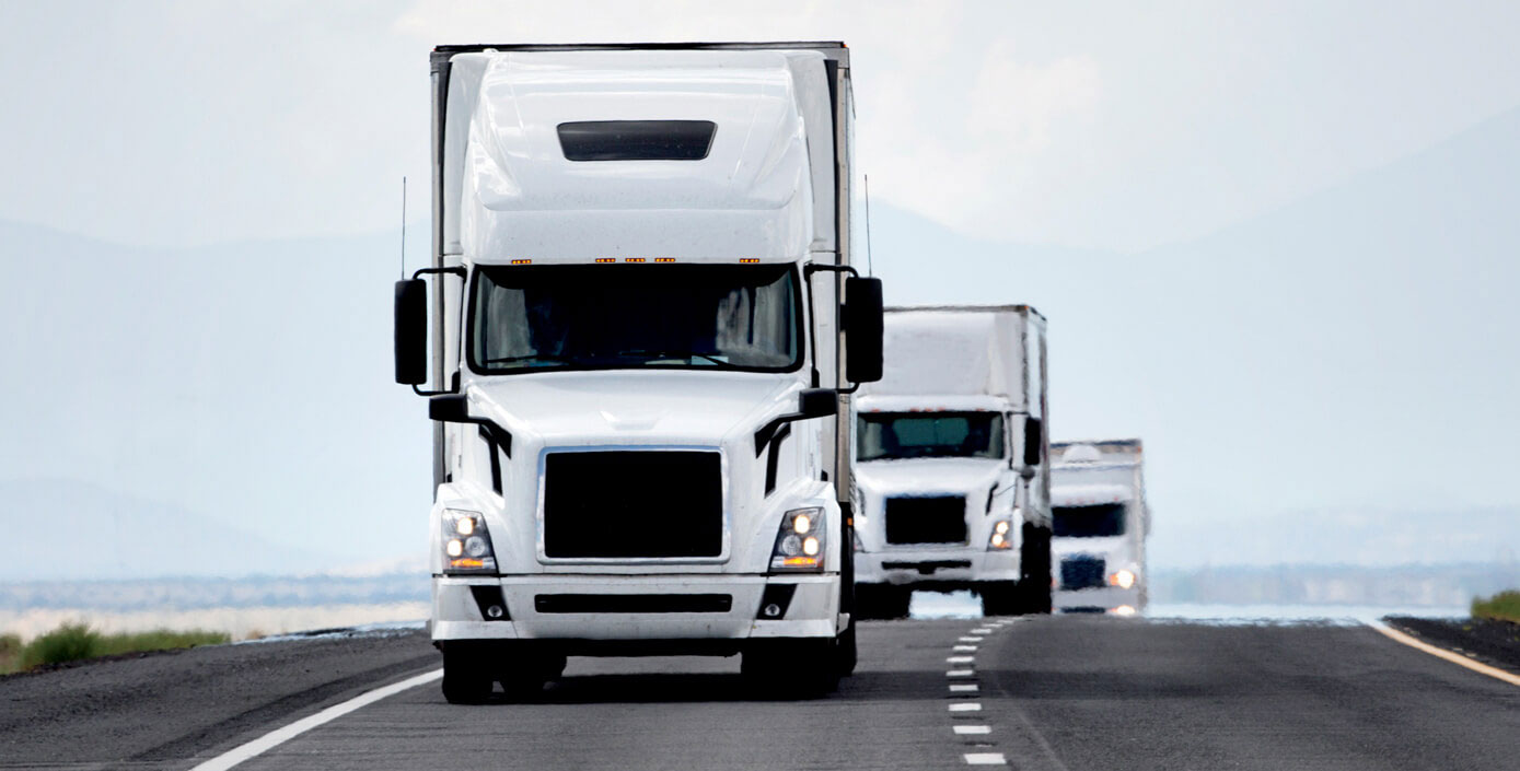 Three white trucks platooning down an open road