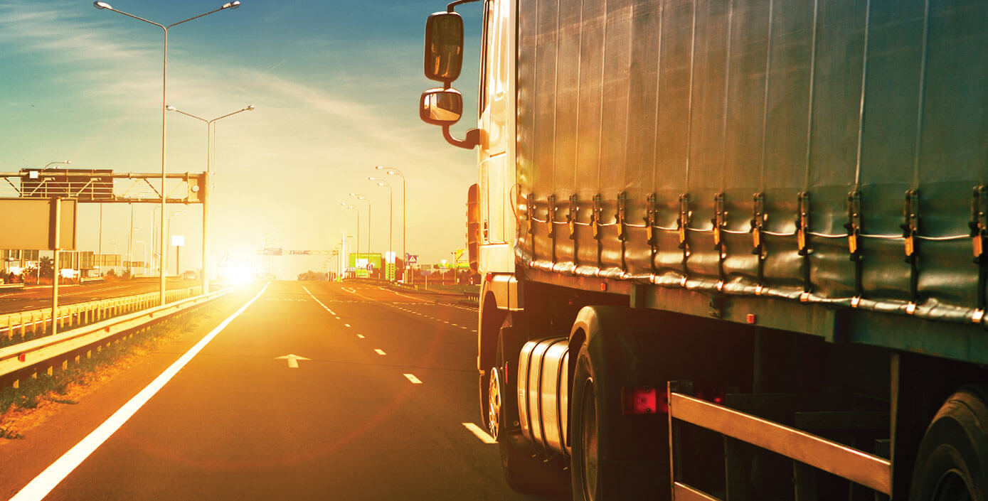 A transport truck on a highway headed towards a sunset. 