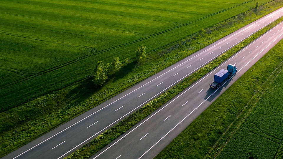 Class 8 truck driving down highway with green pastures surrounding it