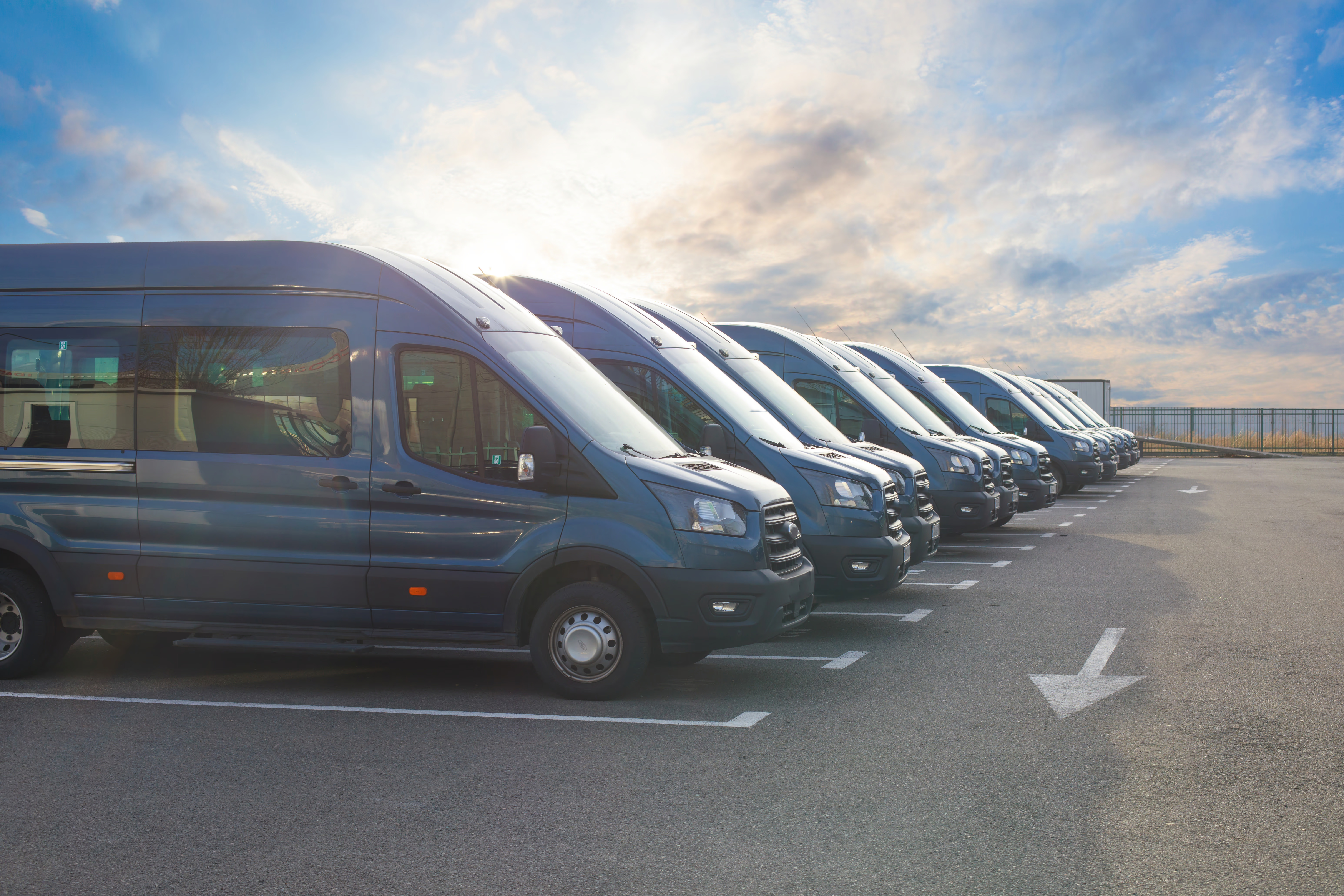 A row of commercial vans parked side by side beneath a bright sky.