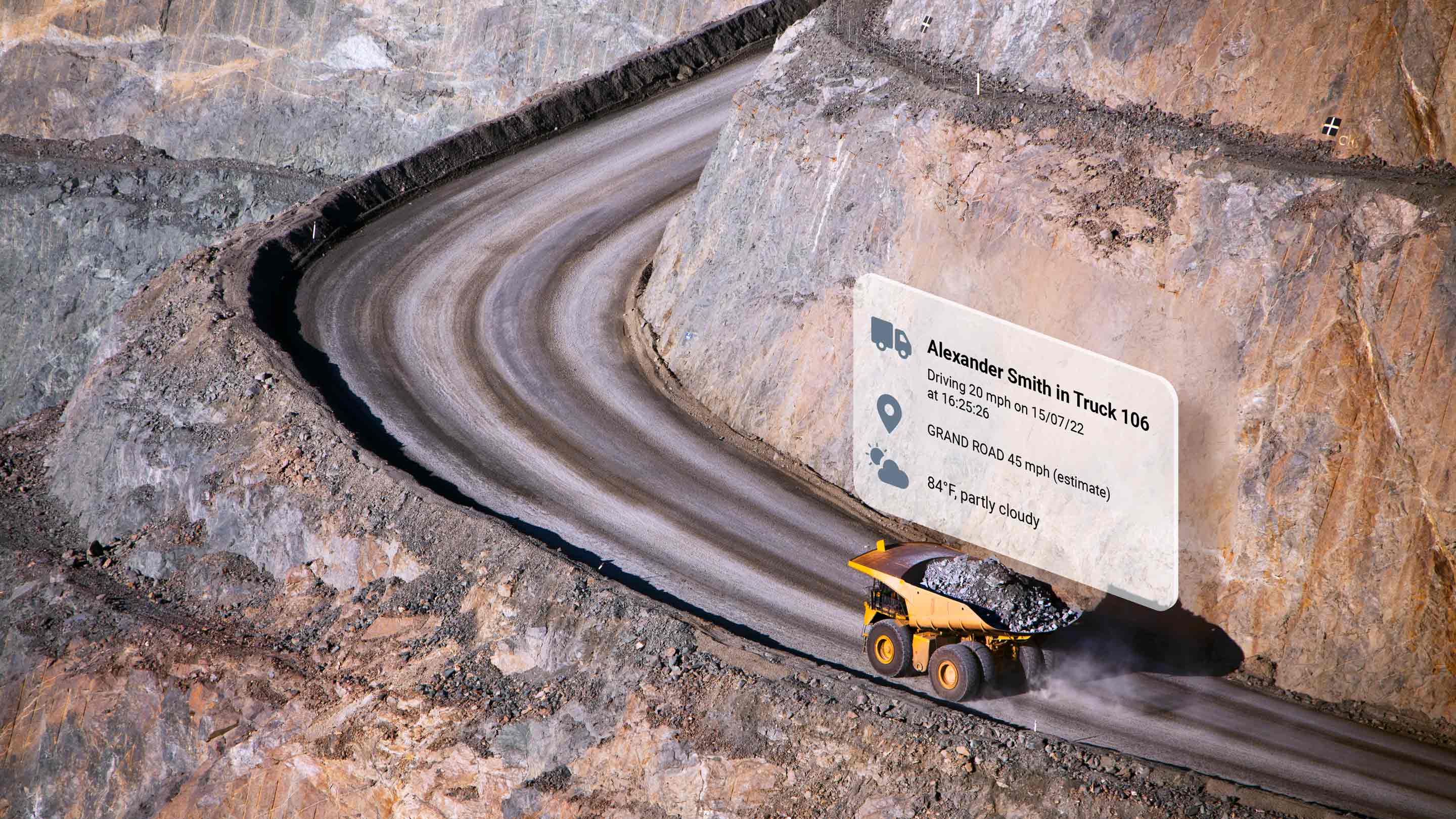 Yellow dump truck driving up a curving dirt road with MyGeotab UI elements above it