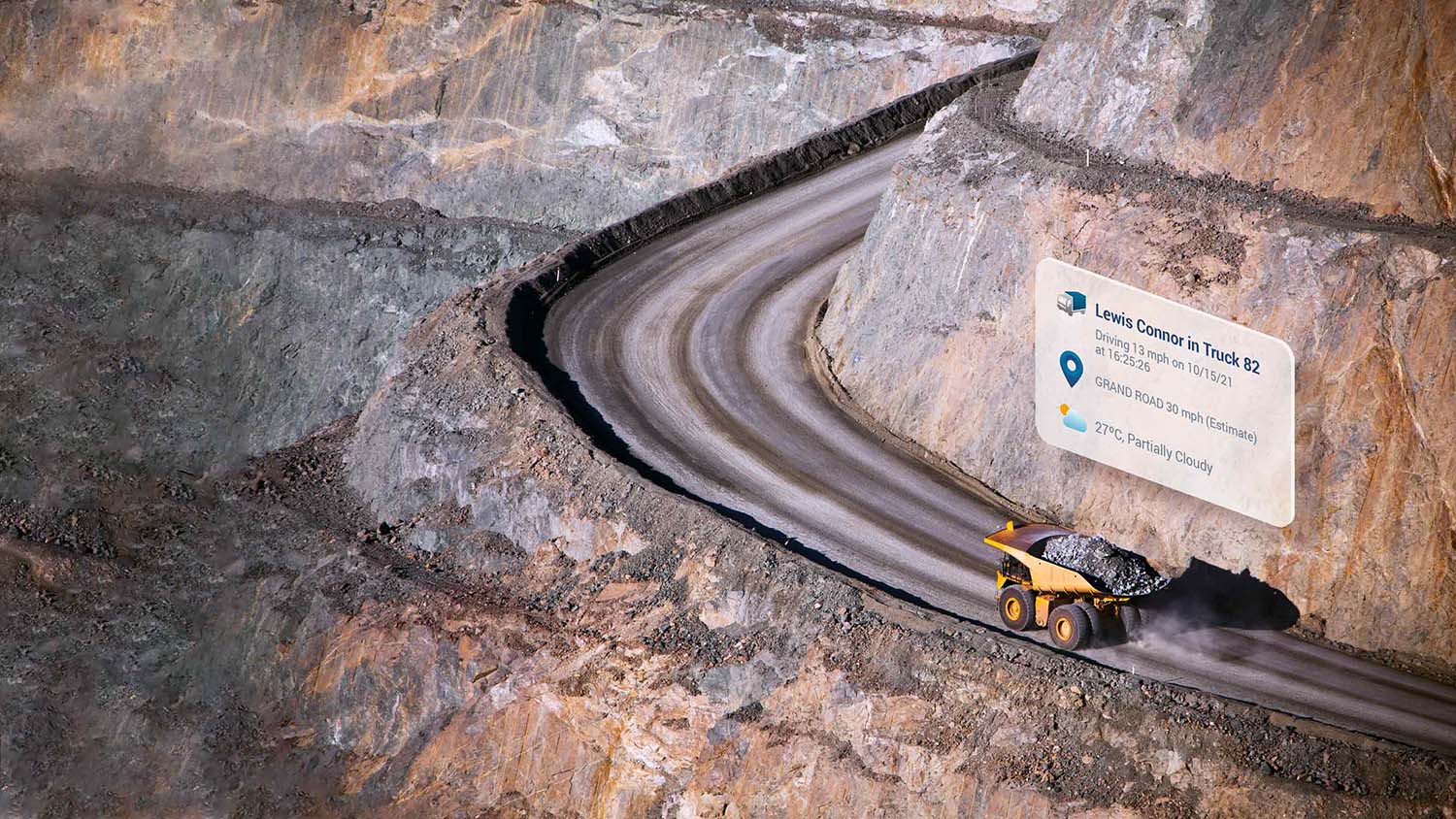 Yellow dump truck driving up a curving dirt road with MyGeotab UI elements above it