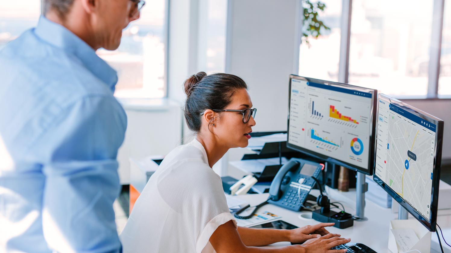 Woman working on two monitors displaying MyGeotab dashboards