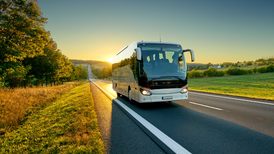 Coach bus driving on road with sunset in background