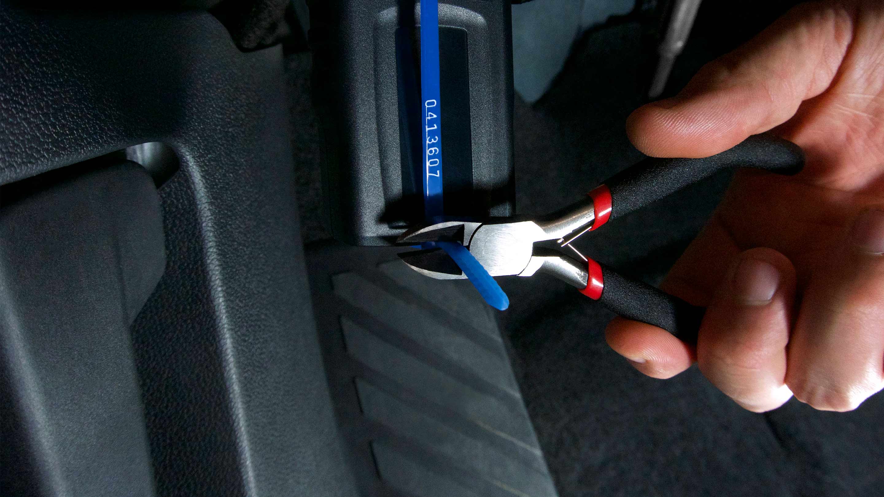 A hand holding pliers cutting a blue zip tie